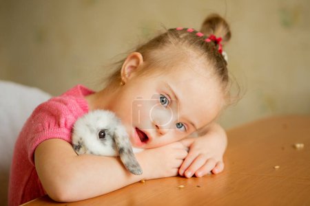 Photo for Beautiful little girl with Down syndrome tenderly hugs a rabbit - Royalty Free Image