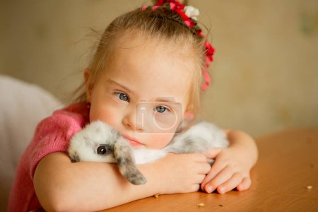 Téléchargez les photos : Beautiful little girl with Down syndrome tenderly hugs a rabbit - en image libre de droit