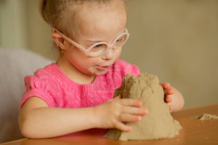 Photo for A girl with Down syndrome plays with colorful kinetic sand - Royalty Free Image
