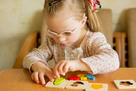 Téléchargez les photos : A girl with Down syndrome develops fine motor skills. learning to assemble puzzles - en image libre de droit