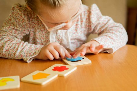 Téléchargez les photos : A girl with Down syndrome develops fine motor skills. learning to assemble puzzles - en image libre de droit
