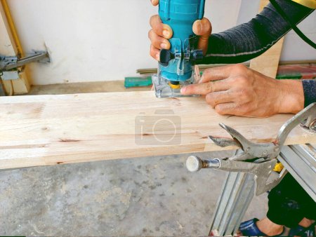 Téléchargez les photos : Gros plan travailleur en utilisant un routeur en bois électrique faisant modèle de beauté sur le bois partie de meubles fabriqués à la main - en image libre de droit