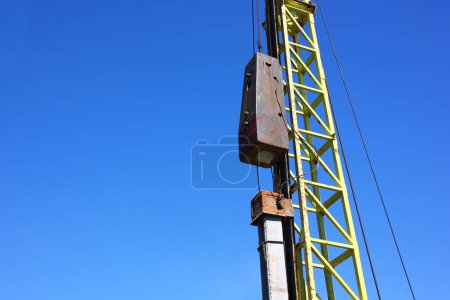 Téléchargez les photos : Grue de battage de pieux travaillant sur chantier contre ciel bleu - en image libre de droit