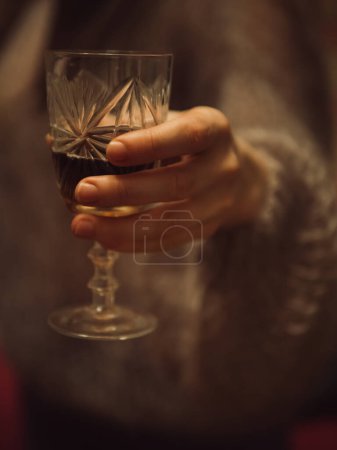 Primer plano vertical de una mano de mujer sosteniendo una copa de vino tinto.