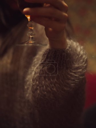 Téléchargez les photos : Plan vertical rapproché d'une main de femme dans un délicat pull tricoté violet tenant un verre de vin. - en image libre de droit