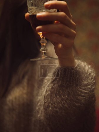 Vertical close up shot of a womans hand in a delicate purple knitted sweater holding a glass of wine.