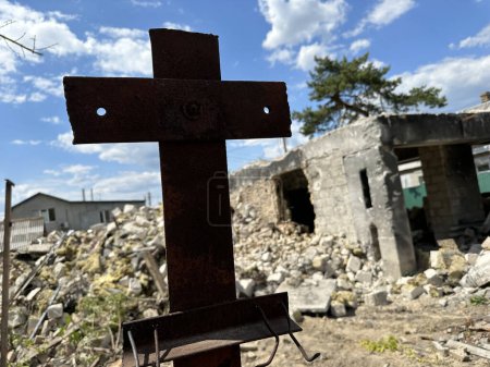 The ruins of a residential building after shelling. Cross on the background of a burnt house. Concept: Cross of Christ, suffering from war.