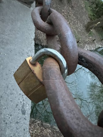 A small padlock is attached to the chain. The lock is attached to a rusty chain. Concept: love is eternal, we are inseparable together.