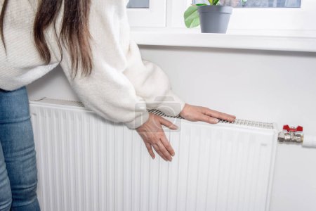 Téléchargez les photos : A woman warms her hands over a heater. Warm and cozy home on cold winter days. - en image libre de droit