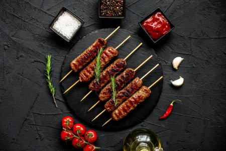 Photo for Grilled sausages with spices and herbs on a black stone background - Royalty Free Image