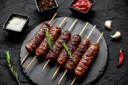 Photo for Grilled sausages with spices and herbs on a black stone background - Royalty Free Image