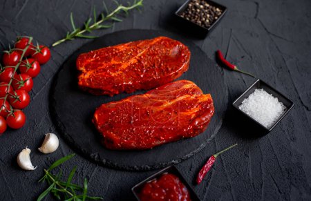 Téléchargez les photos : Steak de bœuf cru aux épices et herbes sur fond noir - en image libre de droit