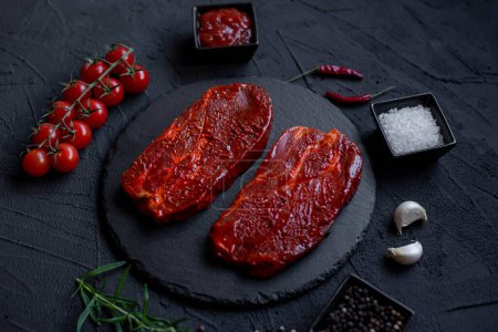 Téléchargez les photos : Steak de bœuf cru aux épices et herbes sur fond noir - en image libre de droit