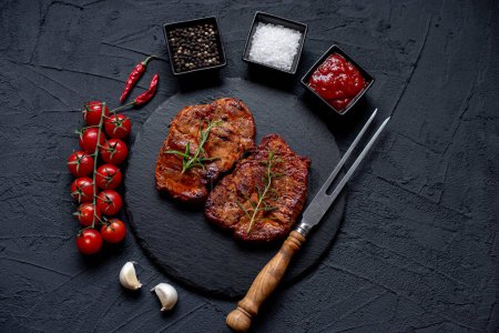 Téléchargez les photos : Steak de bœuf grillé aux légumes et épices sur fond noir - en image libre de droit