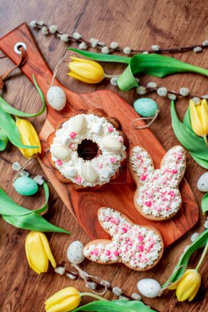Photo for Decorative eggs, gingerbread cookie, willow twigs and yellow tulips on a wooden board - Royalty Free Image