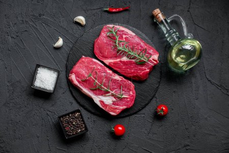 Téléchargez les photos : Steaks de bœuf cru aux épices et herbes sur fond noir - en image libre de droit