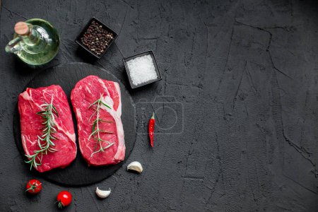 Photo for Raw beef steaks with spices and herbs on black background - Royalty Free Image