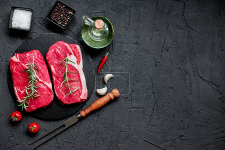 Foto de Filetes de carne cruda con especias y hierbas sobre fondo negro - Imagen libre de derechos