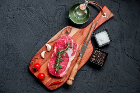Téléchargez les photos : Steak de bœuf cru avec épices et herbes sur fond noir. vue de dessus - en image libre de droit