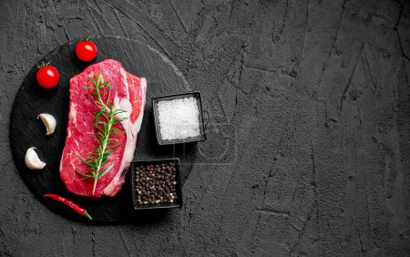 Téléchargez les photos : Steak de bœuf cru avec épices et herbes sur fond noir. vue de dessus - en image libre de droit