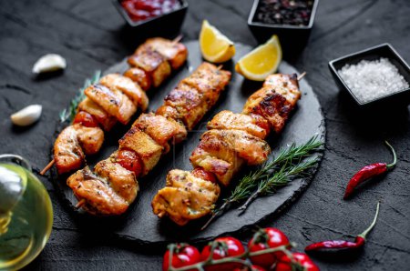 grilled chicken on skewers with vegetables and spices on a black stone background