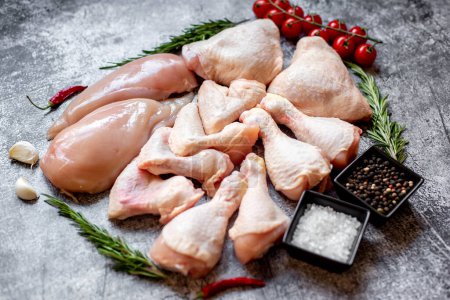 Set of raw chicken fillets, thighs, wings and legs on a stone background