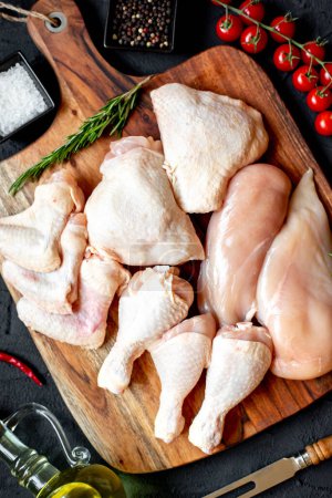Foto de Conjunto de filetes de pollo crudo, muslos, alas y patas sobre tabla de madera - Imagen libre de derechos