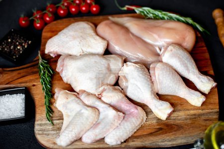 Photo for Set of raw chicken fillets, thighs, wings and legs on wooden board - Royalty Free Image