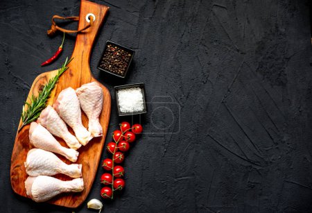 raw chicken legs on black stone background with copy space for your text