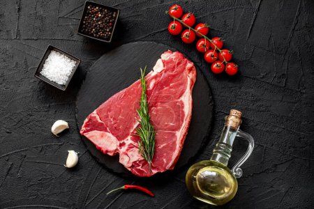 Téléchargez les photos : Steak de boeuf cru avec des épices et des herbes sur fond de pierre noire. vue de dessus. - en image libre de droit