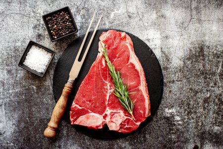Photo for Raw beef steak with spices and herbs on black stone board - Royalty Free Image