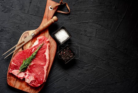 Téléchargez les photos : Steak de bœuf cru aux épices et herbes sur fond noir, espace de copie - en image libre de droit
