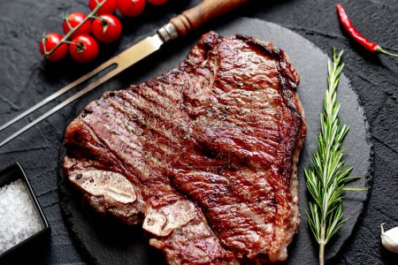 Téléchargez les photos : Steak de bœuf grillé au romarin et épices sur planche de pierre noire - en image libre de droit