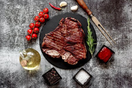 Photo for Grilled beef steak with rosemary and spices on black stone board, top view - Royalty Free Image