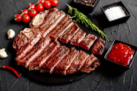 Photo for Sliced grilled beef steak with spices and rosemary on black background - Royalty Free Image
