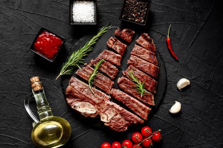 Photo for Sliced grilled beef steak with spices and rosemary on black background, top view - Royalty Free Image
