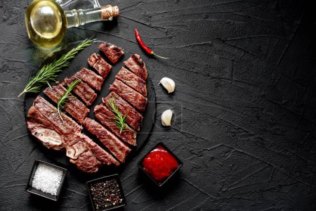 Téléchargez les photos : Steak de bœuf grillé aux épices et romarin haché en morceaux sur fond noir, espace de copie - en image libre de droit