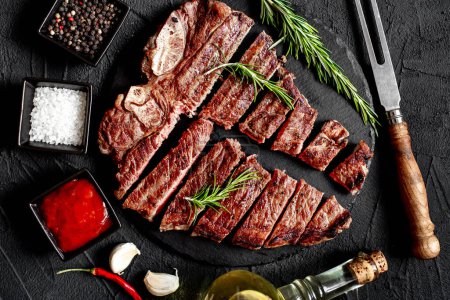 Téléchargez les photos : Steak de bœuf grillé tranché aux épices et romarin sur fond noir - en image libre de droit