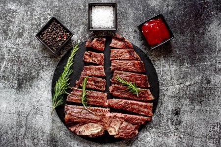 Téléchargez les photos : Steak de bœuf grillé aux épices et romarin haché en morceaux sur un panneau de pierre noire - en image libre de droit