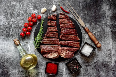 Photo for Grilled beef steak with spices and rosemary chopped into pieces on black stone board - Royalty Free Image