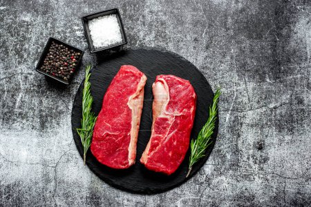 Photo for Raw beef steak with spices and herbs on black stone background - Royalty Free Image