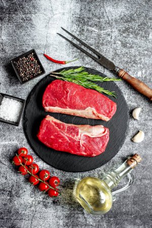 Téléchargez les photos : Steak de bœuf cru aux épices et herbes sur fond de pierre noire - en image libre de droit