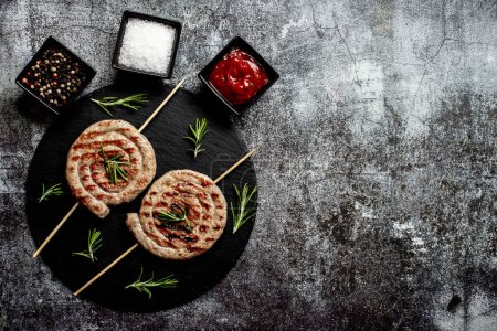 Photo for Grilled rolled chicken sausages on skewers with spices and herbs, close up view - Royalty Free Image