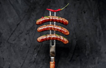 Téléchargez les photos : Saucisses grillées avec du poivre sur la fourchette. fond noir - en image libre de droit