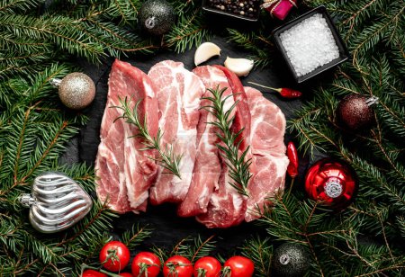 Foto de Filetes de cerdo crudos con decoraciones navideñas sobre fondo de piedra - Imagen libre de derechos