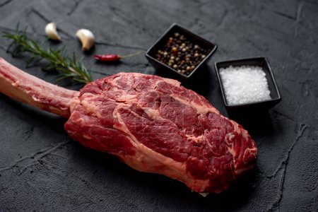 Photo for Raw Tomahawk steak and spices on black stone background - Royalty Free Image