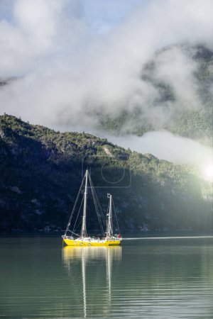 Photo for Yellow boat floating on the water on foggy morning day in the mountains. Caleta Tortel, Patagonia, Chile. Vertical photography - Royalty Free Image