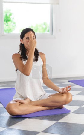 Photo for Latin woman yogi doing Nadi Shoddana Pranayama in half lotus position doing Alternate Nostril Breathing. Breathing exercise for yoga lesson. Vertical photography - Royalty Free Image