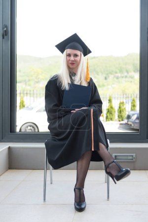 Téléchargez les photos : Femme blonde collège ou lycée diplômé porter confidentiellement casquette noire et robe à l'obtention du diplôme - en image libre de droit