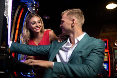 Téléchargez les photos : Jeune Groupe de Personnes à la Machine Automat dans un Casino et Célébrer - en image libre de droit